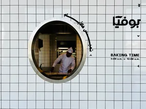 繁忙的麵包店內部，有餐桌、椅子、烤箱，以及一名男子準備食物