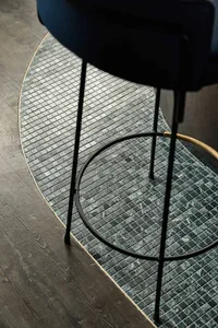 A black chair sits on a stone floor with a unique tile pattern, in a minimalist interior setting