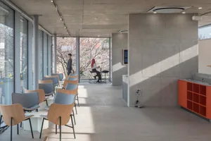 A calm and inviting lobby space with concrete walls and floors, featuring chairs near windows that allow natural light to enter