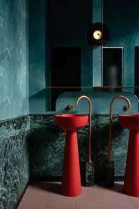 Modern bathroom with two red sinks on a marble countertop, under a large mirror, with a luxurious upscale design