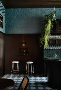 A modern bar with a black countertop, blue walls, and three stools, creating a relaxed and inviting atmosphere