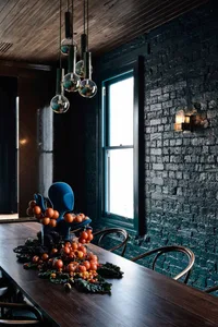 A darkly lit dining space with a table surrounded by chairs, featuring oranges as a pop of color