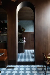 A warm and inviting bar area with wooden walls and floors, featuring a dining table, chairs, and a potted plant, with bottles scattered throughout