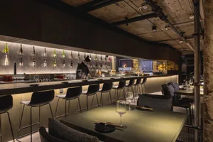 Modern bar area with a long counter, multiple bottles, and seating for patrons