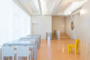 空蕩蕩的餐廳，配有黃色餐桌與椅子、水泥地板，以及牆上的時鐘