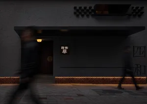 Gray modern building with a man walking towards the camera, another person walking away, and a third person in the background