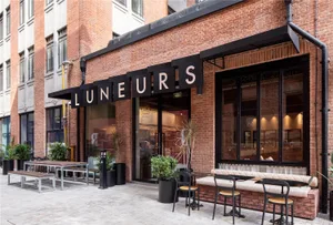 An inviting outdoor cafe with a brick wall, a bench, and chairs in a well-lit area, perfect for dining or enjoying a coffee