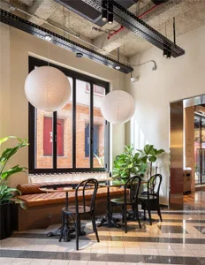 Modern restaurant dining area with white walls, black accents, and natural light from windows, featuring multiple chairs, tables, and a bench