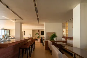 Modern restaurant interior with wooden floors, white walls, and a mix of seating options, including couches and chairs, surrounded by potted plants