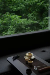 Cozy living space with a black sofa, natural light from a window, and a table with cups, a bowl, and grapes