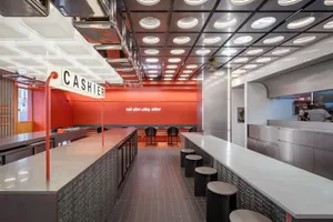 A modern restaurant interior with a cashier area and dining tables, featuring red walls and various chairs