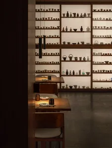 A room filled with bowls and vases on shelves and tables, set against a wooden floor background