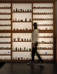 A woman walks past a glass display case filled with vases of various sizes and shapes, arranged in rows for a visually appealing presentation