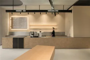 A modern restaurant interior with a counter area, cash register, and coffee machine, lit by overhead lighting