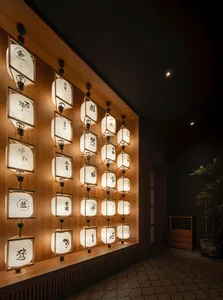 A warm and inviting living space with a wooden wall adorned with numerous small square lanterns, a potted plant, and natural light