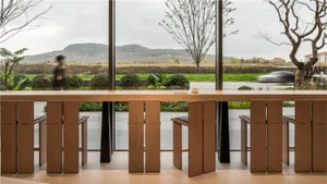 A cozy dining space with a wooden table and chairs in front of a large window, illuminated by natural sunlight