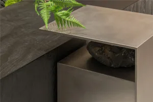 A modern and minimalistic indoor space with a large silver table, two smaller tables, a potted plant, and metallic surfaces