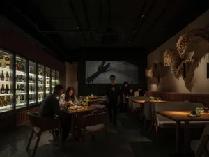熱鬧的室內餐飲空間，設有多張桌子和椅子，人們享用餐點並交談，桌面擺放瓶子