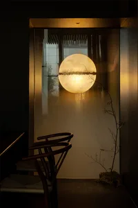 A dimly lit room with a chair in front of a window featuring a reflection of a round object, creating an interesting visual effect