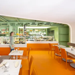A warm and inviting dining area with orange walls, wooden tables and chairs, and wine glasses on the tables
