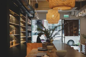 A cozy cafe interior with a counter displaying bowls, cups, and vases, and a person attending to customers
