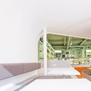 A casual restaurant interior with a large concrete wall, tables, chairs, bottles, and wine glasses, creating a relaxed atmosphere for socializing and dining