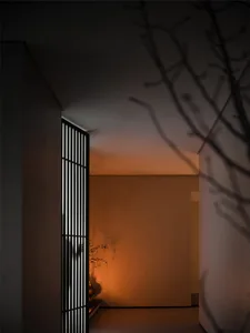 A modern hallway with concrete walls, a window, and two doors, lit by warm lighting that casts shadows on the walls
