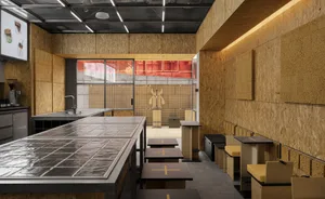 A modern kitchen with wooden walls and floors, featuring several tables and chairs, and a stylish atmosphere