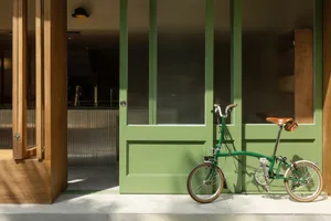 A casual entrance with a wooden door and a bicycle parked outside, accompanied by two bottles near the bike