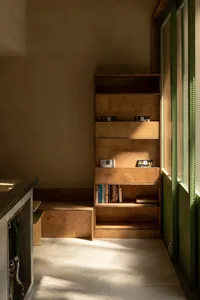 A cozy living area with a wooden bookshelf in front of a window, surrounded by books and a bench for reading or relaxation