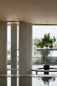 A well-lit living area with chairs, a dining table, and a potted plant, surrounded by natural light from a large window