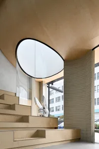 A modern interior space with a large glass window, wooden structure, and two staircases, featuring a chair and natural light