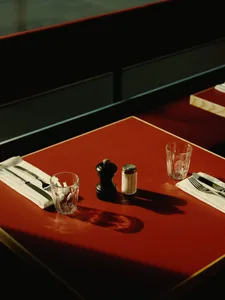 A dining area with red tables and chairs, featuring glasses, a salt shaker, pepper shaker, and a bottle, set in a cozy and inviting atmosphere