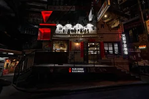 A bustling Asian restaurant in a city at night with a red sign, dining tables, and chairs