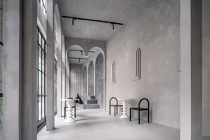 Empty white room with high ceilings, an archway, two chairs, and a dining table, exuding a minimalist and clean atmosphere