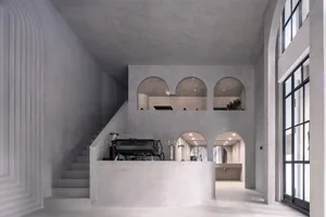 An open-plan living area with a staircase, a dining table, and a chair, with two people standing in the room