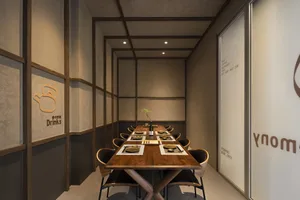 A warm and inviting restaurant interior with a large dining table, wooden furniture, and potted plants, set against neutral-toned walls