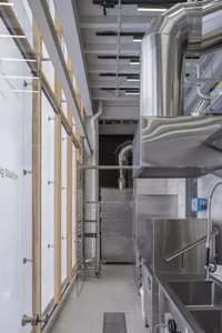 Industrial kitchen with stainless steel appliances and fixtures, featuring multiple ovens and sinks in a functional and professional environment