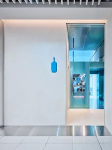 A modern restaurant interior with a counter, glass, and wood, featuring a man standing in front of the counter with two bottles on display
