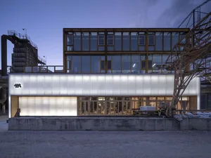 A modern building with a sleek design featuring white and grey elements, glass, and concrete, with a dynamic arrangement of windows across the facade