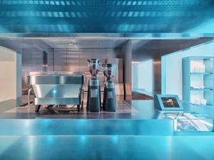 Well-lit modern kitchen with a silver coffee maker, black blenders, and natural light from windows