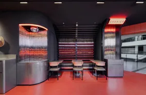 A modern restaurant interior with red walls, tables, chairs, and ample seating options