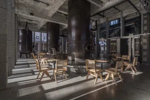 Industrial cafe with cylindrical tanks, chairs, and dining tables, surrounded by benches for social seating