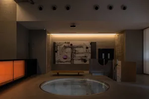 Luxurious interior space with a circular pool, benches, chairs, dining tables, and potted plants