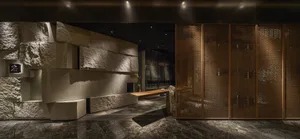 Dimly lit room with a stone wall, wooden doors, and a bench, featuring two potted plants