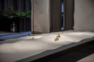 A modern space with a white concrete wall featuring two golden statues at different heights, creating an artistic focal point