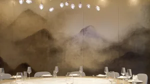 Dining area with a round table, wine glasses, cups, utensils, and bottles, set in a sophisticated and inviting environment