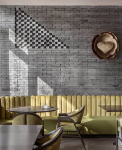 A restaurant interior with yellow walls, grey floors, and various chairs around dining tables, creating a cozy atmosphere with good lighting