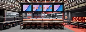 A modern restaurant with a counter and stools, featuring red and black decor, TV screens, and a welcoming atmosphere