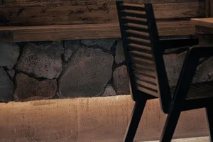 A serene indoor space with a wooden chair next to a stone wall, with a calm atmosphere